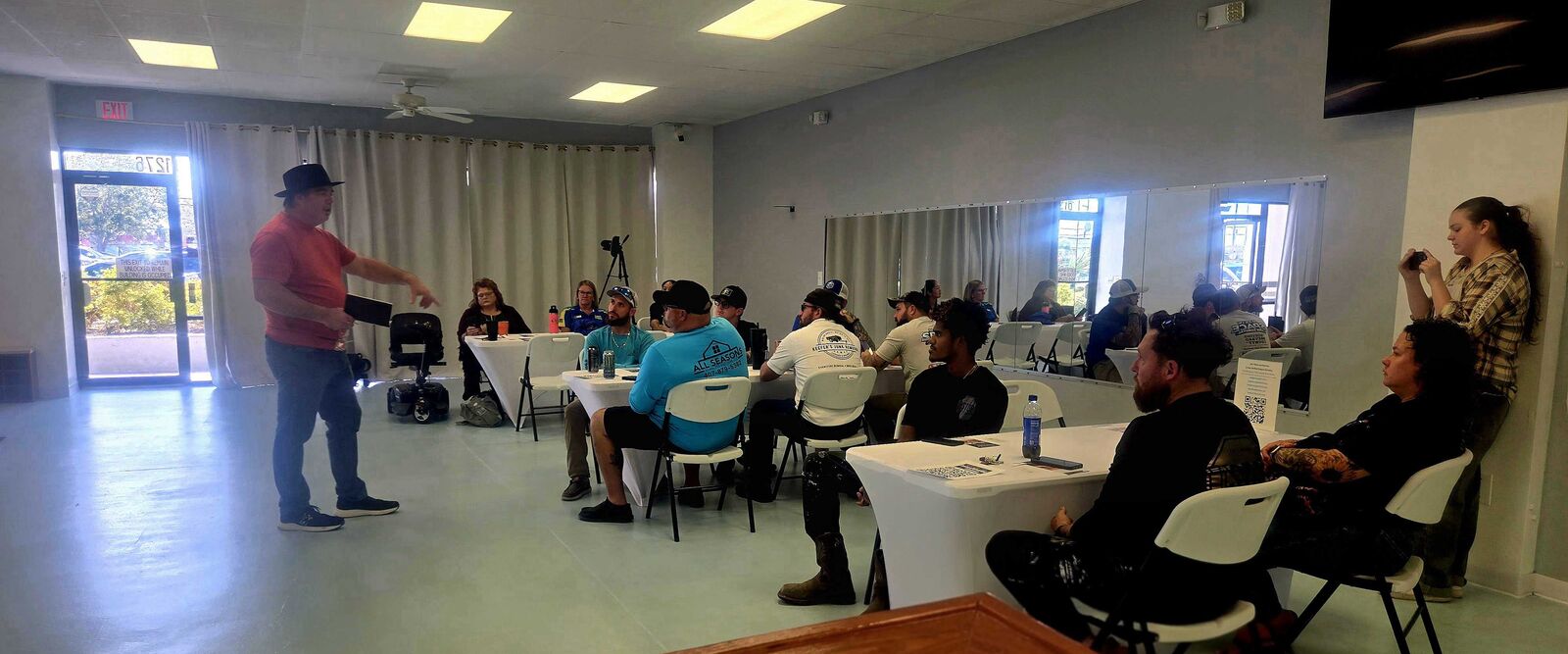 A speaker gestures toward a seated audience in bright rooms